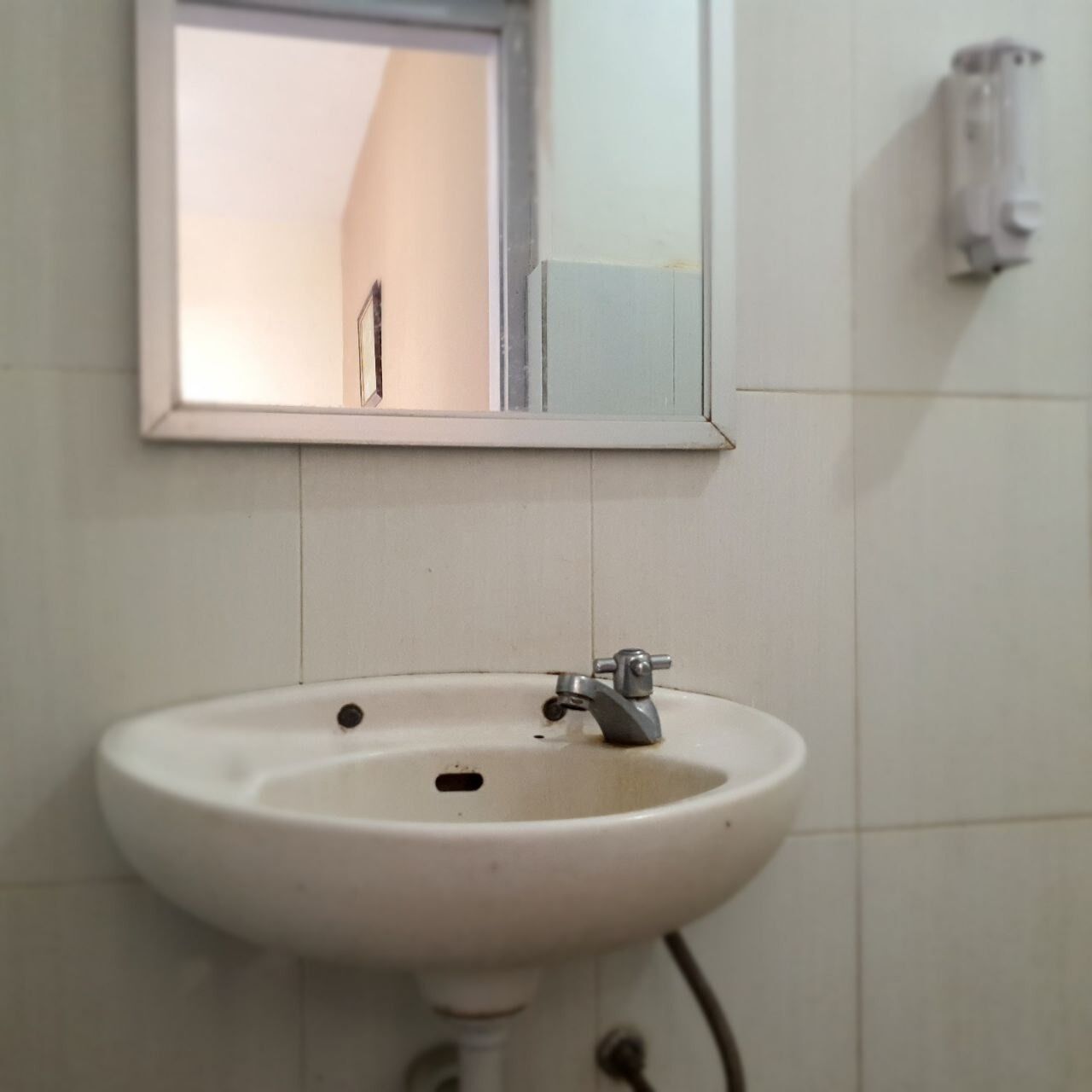 A white bathroom sink with a mirror above it, a towel rack on the wall, and a soap dispenser to the right.