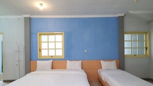 Una habitación con dos camas individuales, un cabecero de madera, un ventanal con marco amarillo y una lámpara en el techo.