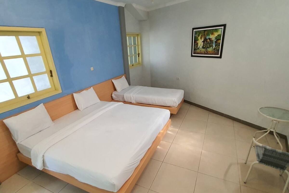 A room with two beds, a small table, and a window with a yellow frame.