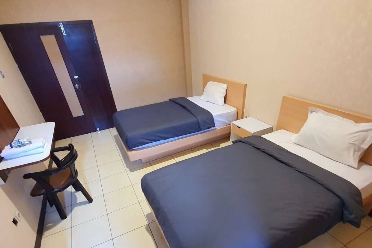 A small hotel room with two beds, a desk, and a chair.