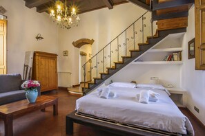 A hotel room with a bed, a wooden coffee table with a vase of flowers, a staircase with a railing, and a chandelier. - Villa Bellesi - Sweet Dreams in Florence (Firenze)