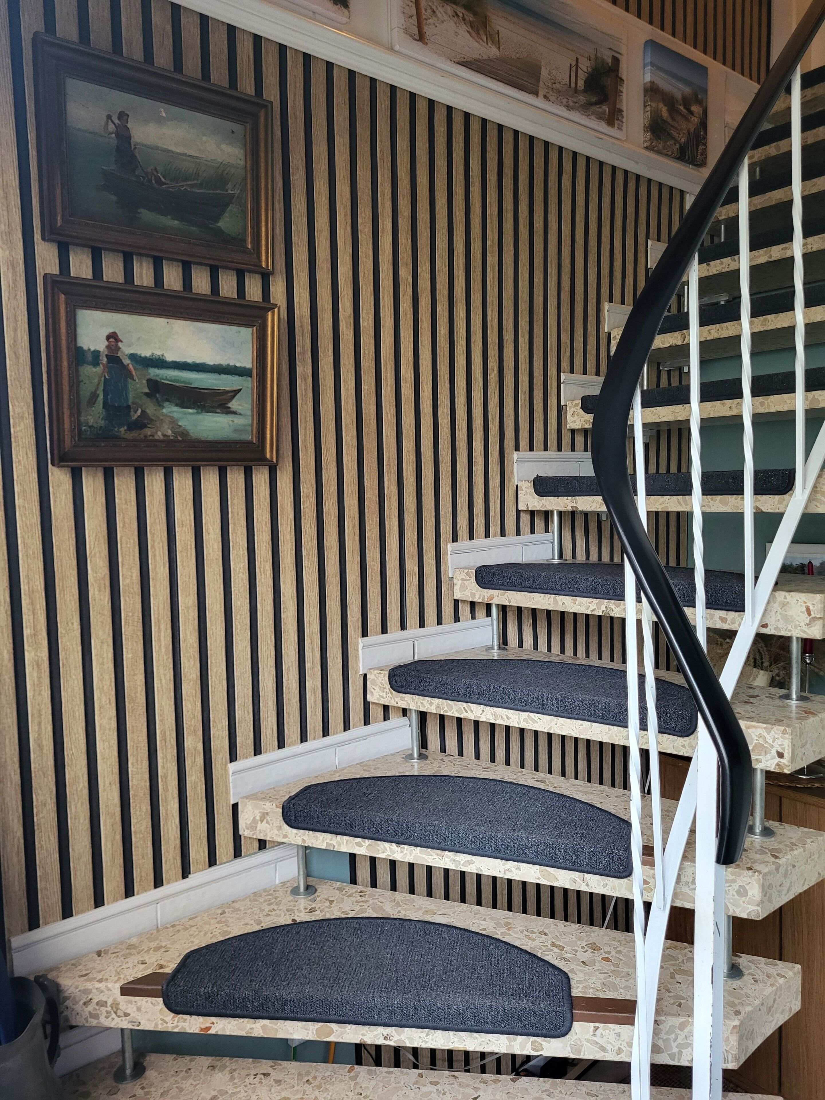 Una escalera en espiral con un muro de madera y dos cuadros enmarcados.