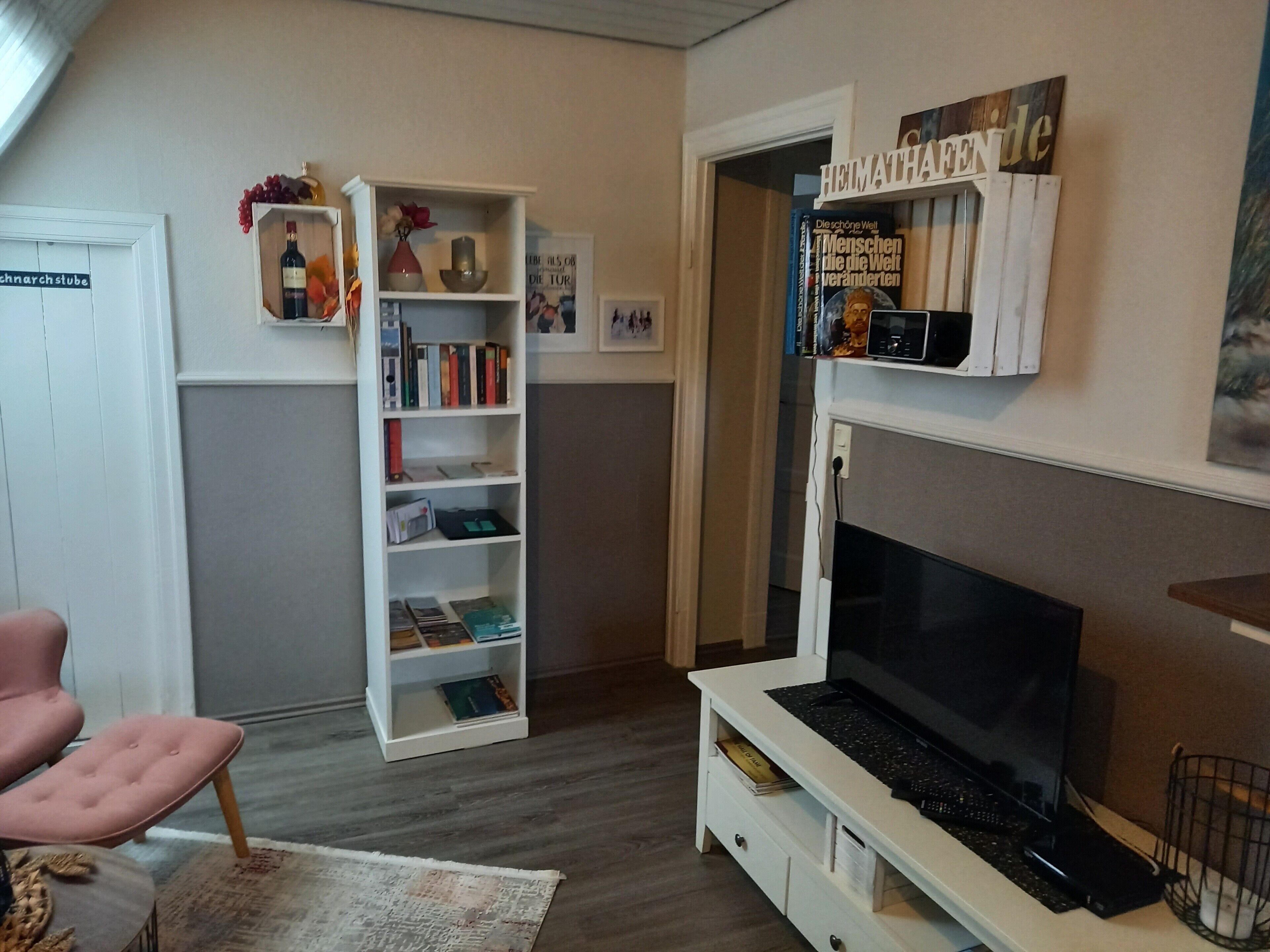 Un salon comprenant un téléviseur, des étagères, un fauteuil rose et un panneau décoratif mural.