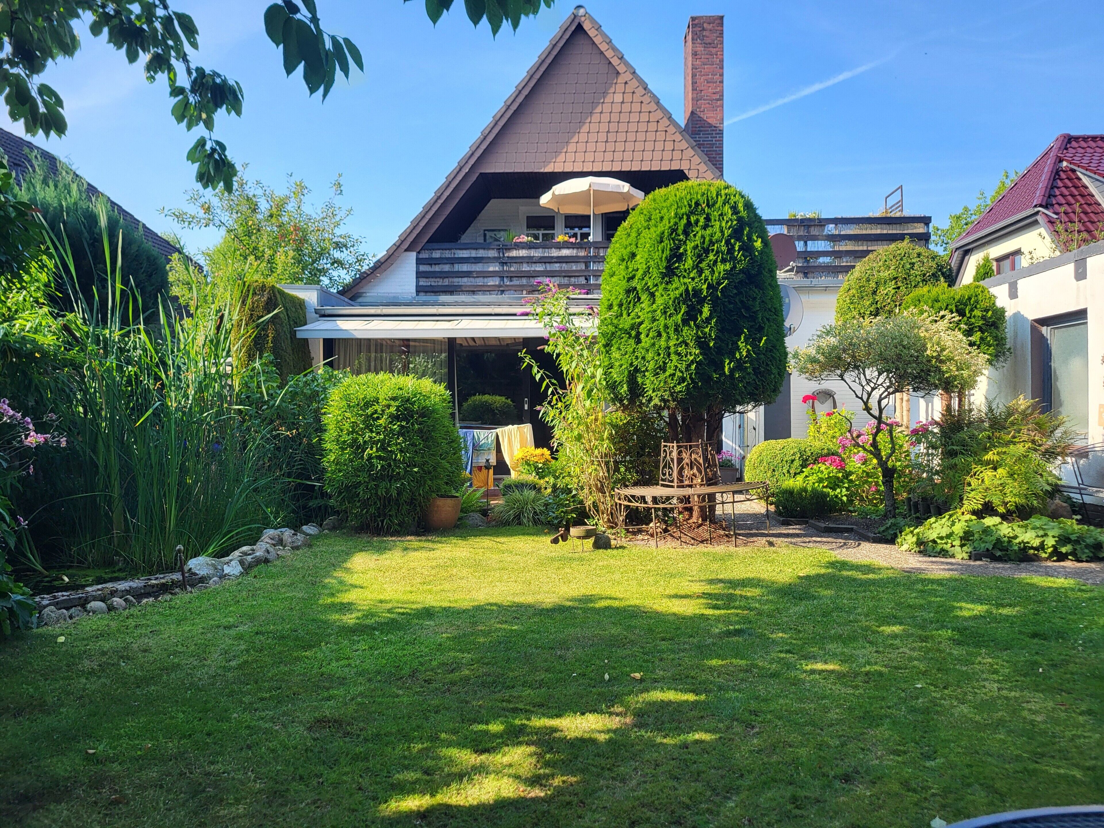 Ein Wohnhaus mit gepflegtem Rasen, einer Terrasse mit Gartenmöbeln und verschiedenen Pflanzen und Sträuchern.