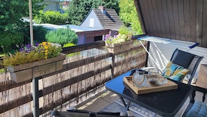 Ein Balkon mit Tisch, Stühlen, einer Hängesessel, einer hängenden Pflanze und Blick ins Viertel.