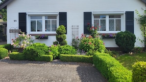 Ein weißes Haus mit schwarzen Fensterläden, Hausnummer 49, und ein gepflegter Garten mit Hecken und Blumen.