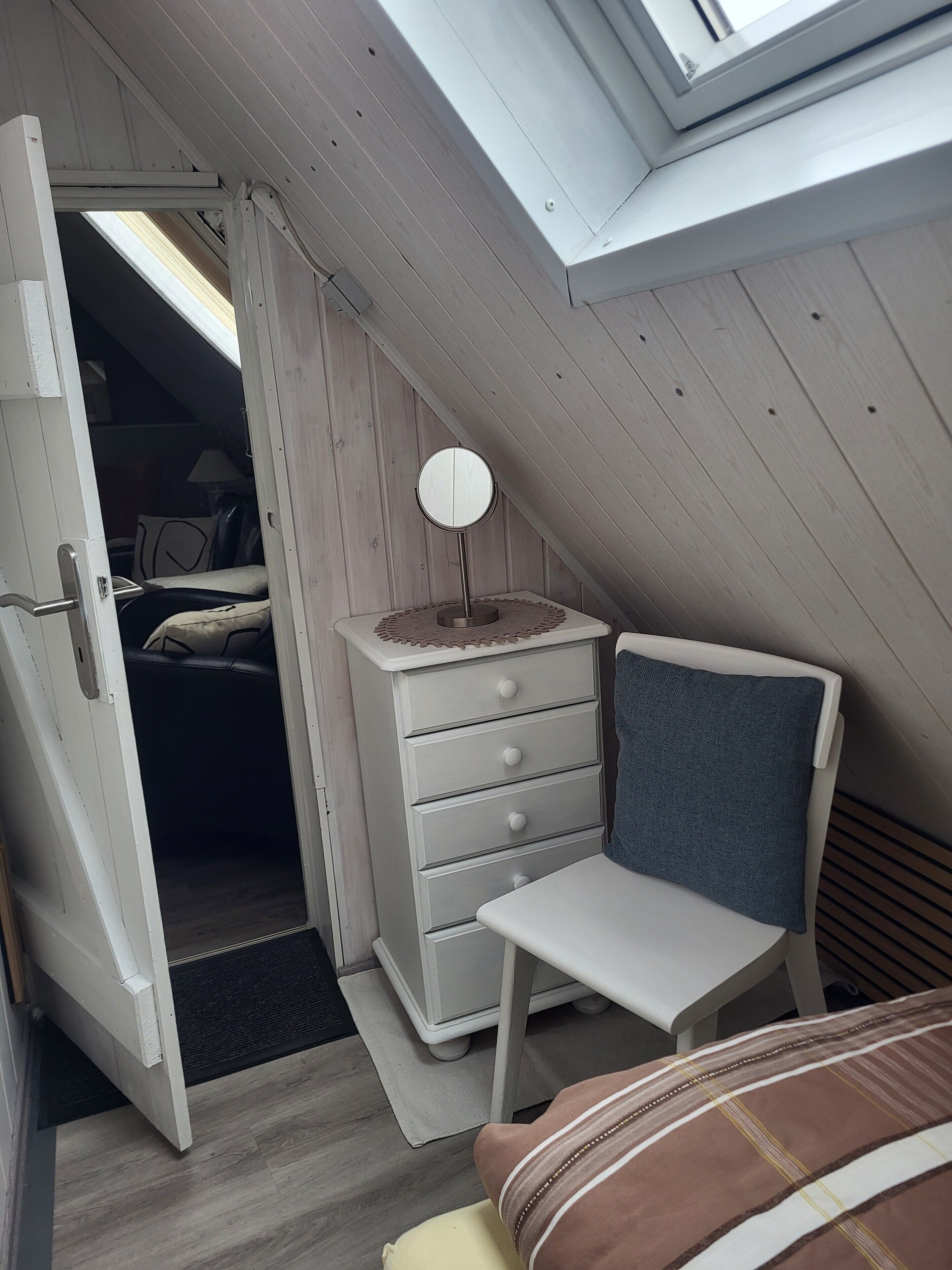 Ein Schlafzimmer mit Oberlicht, Nachttisch, Stuhl und Kommode.