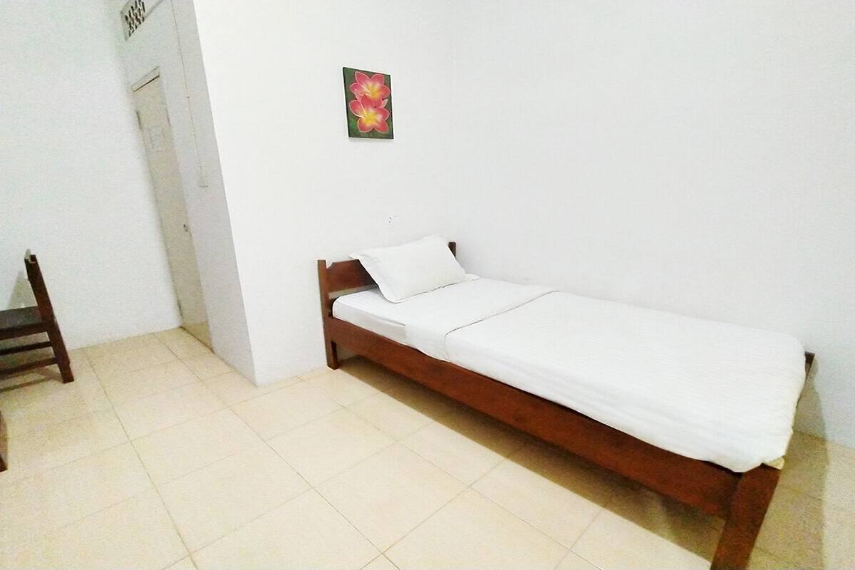 A single bed with a wooden frame and white bedding in a room with white walls and tiled floor.
