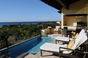 Un espace aménagé au bord de la piscine, avec des chaises longues, un barbecue et une vue sur l’océan.