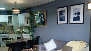 Ein modernes Wohnzimmer mit grauem Sofa, schwarzen Sesseln, einem weißen Couchtisch und einem Essbereich mit Glastisch und Stühlen.