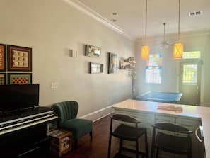 Ein Wohnzimmer mit einem Klavier, einem grünen Sessel, einem Billardtisch und einer Küchenzeile mit Barhocker.