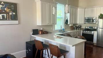 A kitchen with white cabinets, a central island with stools, a stove, and a refrigerator.