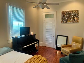 Ein Zimmer mit Klavier, Fernseher, Bett, Sessel und Deckenventilator.