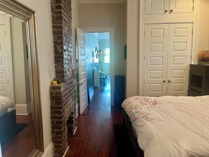 A bedroom with a large bed, a brick wall, and a door leading to a hallway.