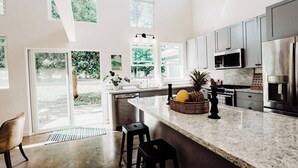 Una cocina moderna con una isla grande, electrodomésticos de acero inoxidable y vistas a zonas verdes.