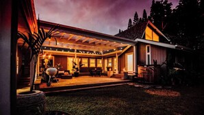 Un patio techado al aire libre con una parrilla, asientos y vistas de la casa.