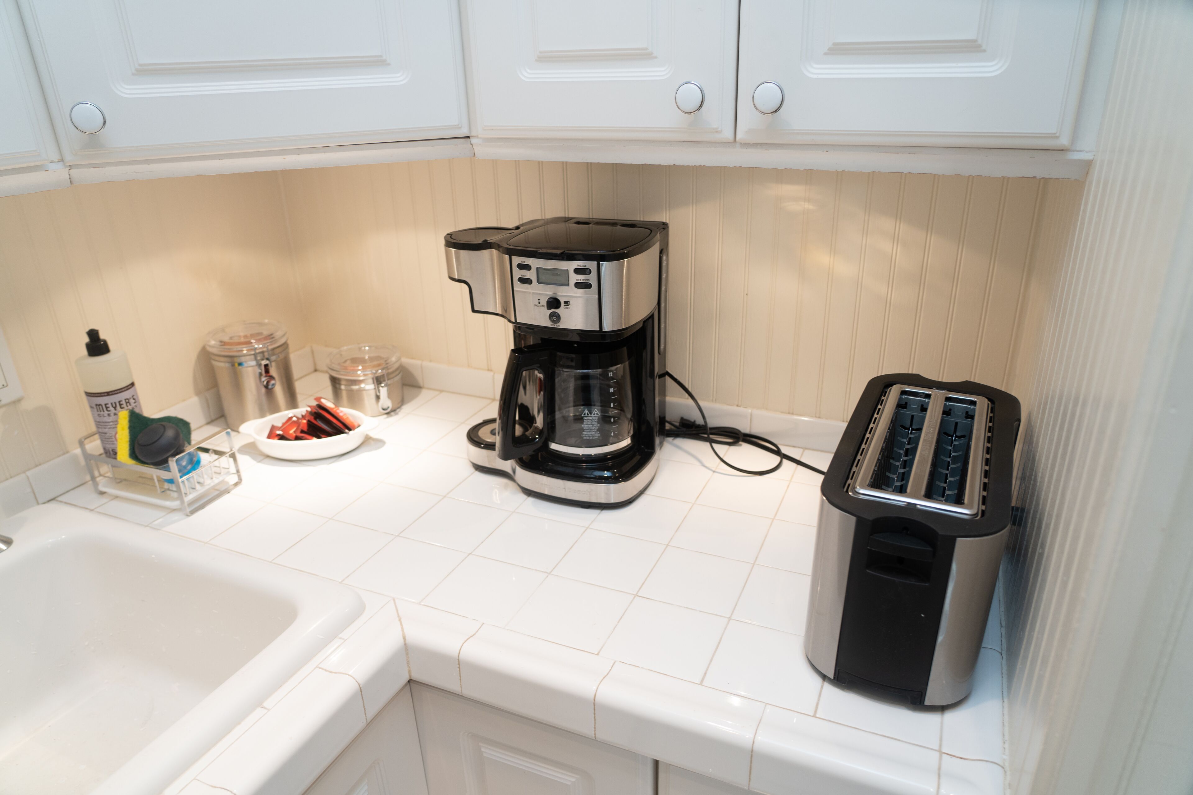 A kitchen with white cabinets, a coffee maker, a toaster, and a sink.
