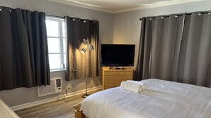 Une chambre d’hôtel avec un lit, une télévision, une table de chevet, une lampe et une fenêtre avec des rideaux.