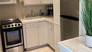 Une cuisine avec des meubles blancs, un four en acier inoxydable, un four à micro-ondes, une machine à café et un réfrigérateur.
