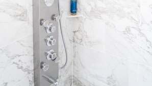 Une douche moderne dotée d’un pommeau de douche à pluie, de plusieurs robinets de contrôle et d’un distributeur de savon fixé sur un mur recouvert de carreaux de marbre.