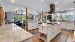Une cuisine spacieuse avec des meubles blancs, un îlot central et une vue sur l’extérieur.