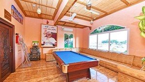 A pool table in a room with a wooden ceiling, a sofa, and a window with a view of the outside. - OYO 139 Al Ghadeer Hotel Apartments (Barka)