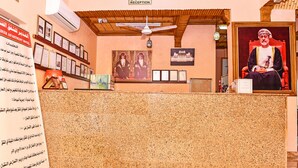 A hotel reception area with a reception desk, framed certificates, a ceiling fan, and a large portrait of a historical figure. - OYO 139 Al Ghadeer Hotel Apartments (Barka)