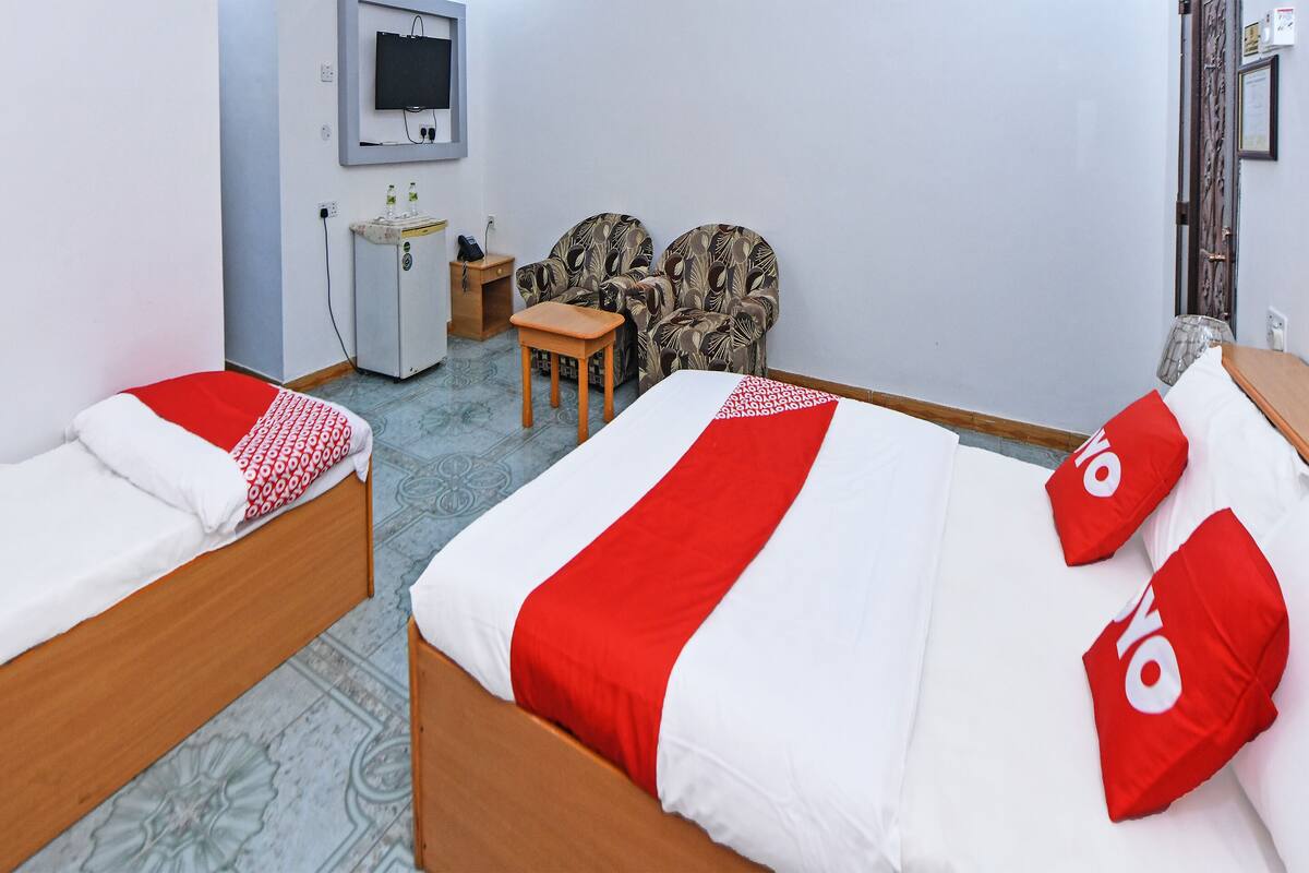 A hotel room with two beds, a desk, a chair, a TV, and a minibar.