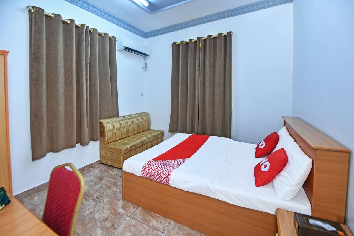 A hotel room with a bed, a sofa, a chair, and curtains.