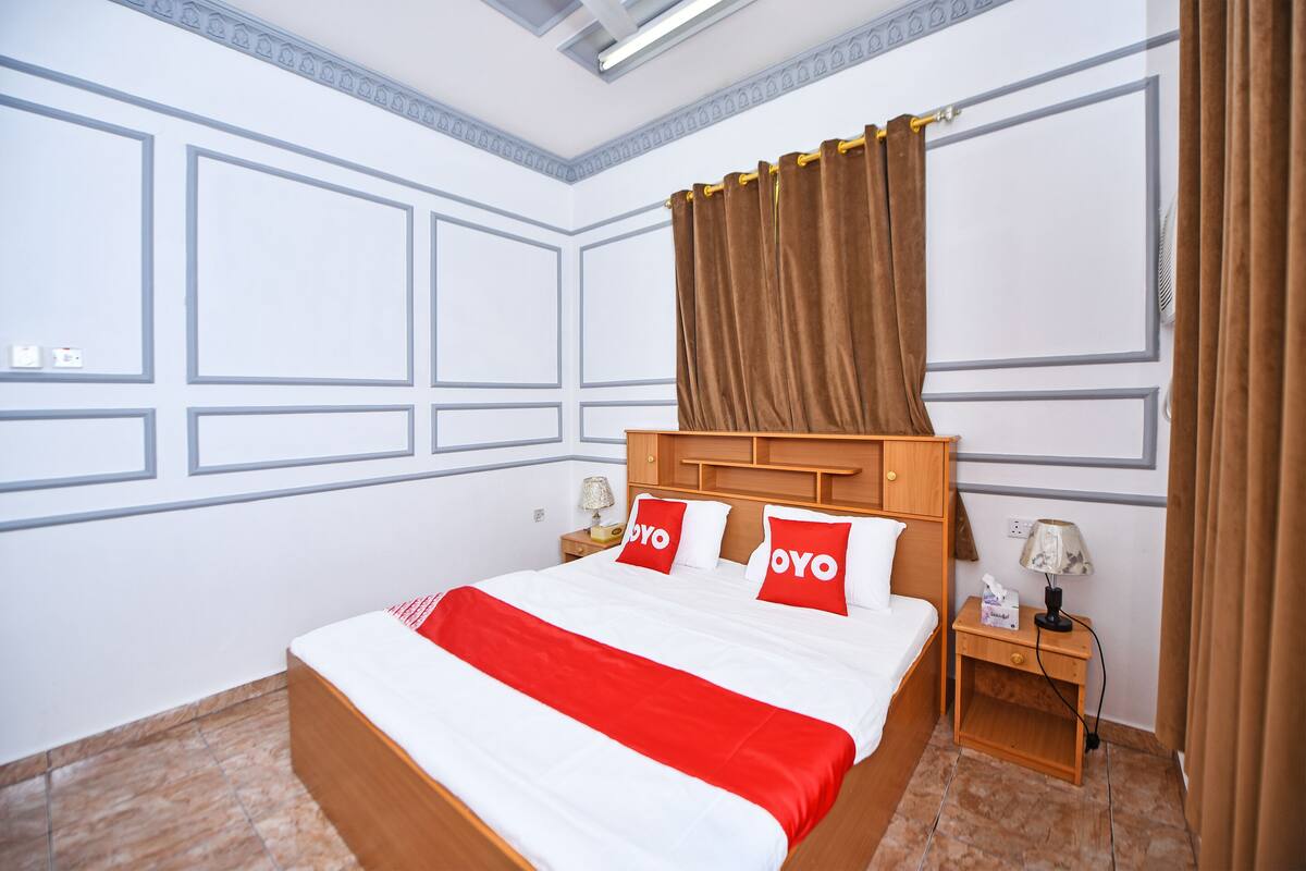 A hotel room with a large bed, two pillows with the brand name, a nightstand with a lamp, and a curtain.