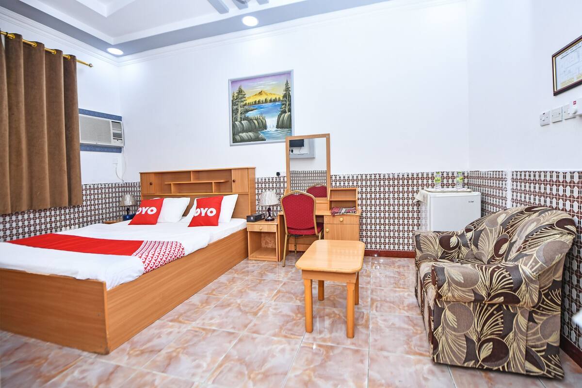 A hotel room with a bed, a desk, a chair, a sofa, and a tiled floor.