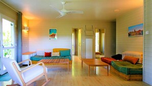 Una sala de estar acogedora con piso de madera, un sillón mecedor, un sofá con cojines de colores, una mesita de centro y un ventilador de techo.