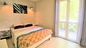 Un dormitorio con cama, mesita de noche, lámpara de pared y un amplio ventanal con cortinas.