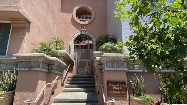 Unos escalones de piedra conducen a una entrada con puerta de hierro y un cartel que dice 'Columbia Place'.