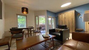 Una sala de estar con un sofá, una mesa de centro, una mesa de comedor con sillas, un sillón de cuero negro y un armario de madera.