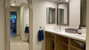Un baño con un espejo grande, dos espejos más pequeños, un lavamanos y un mueble de tocador con repisas abiertas.