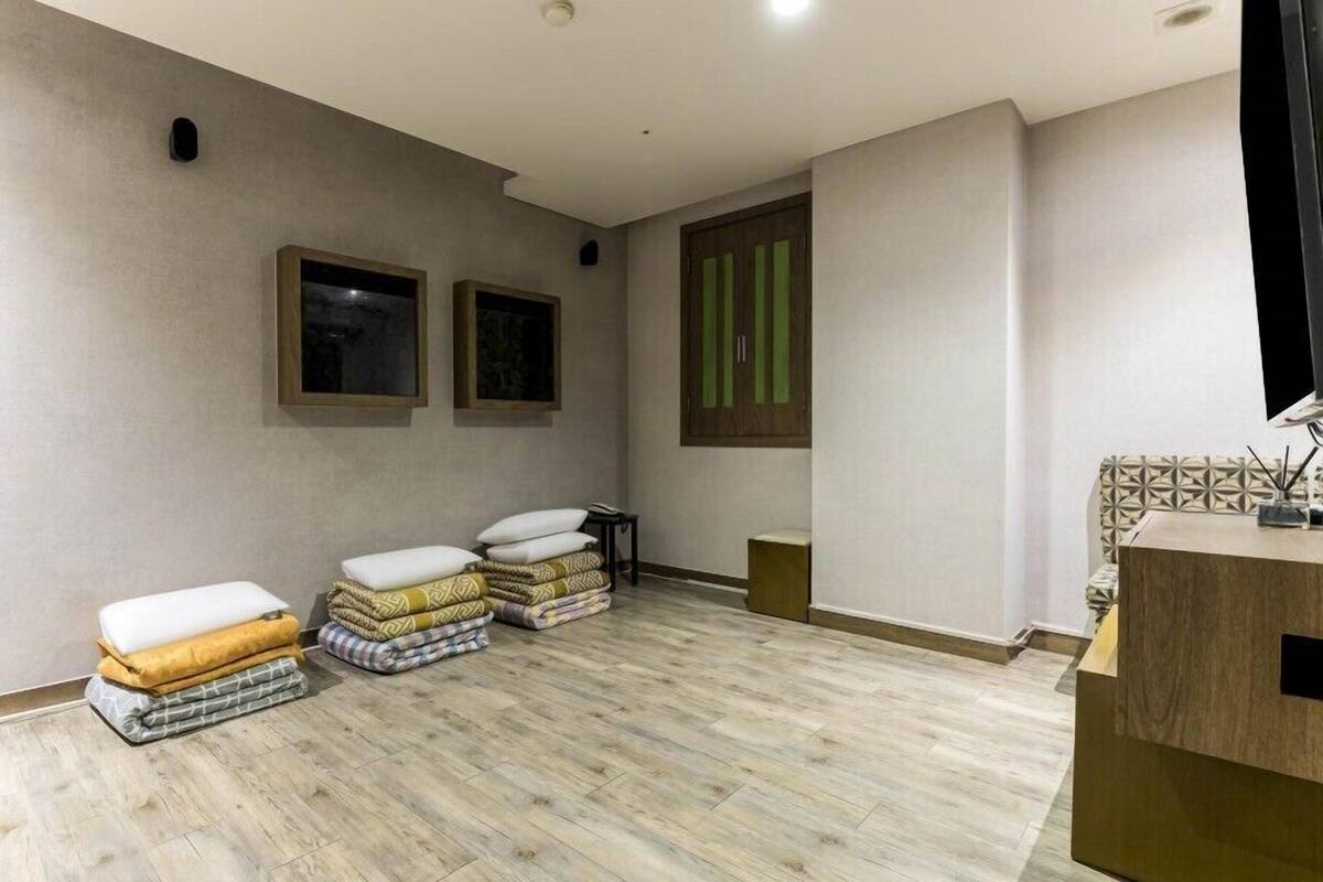 Une pièce avec un plancher en bois, une petite table avec une lampe et deux fenêtres équipées de stores.