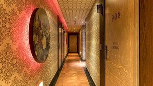 Ein Flur mit strukturiertem Wandpapier, einem großen, runden Kunstwerk und einer Tür mit der Aufschrift „HOTEL BOBOS 908“.
