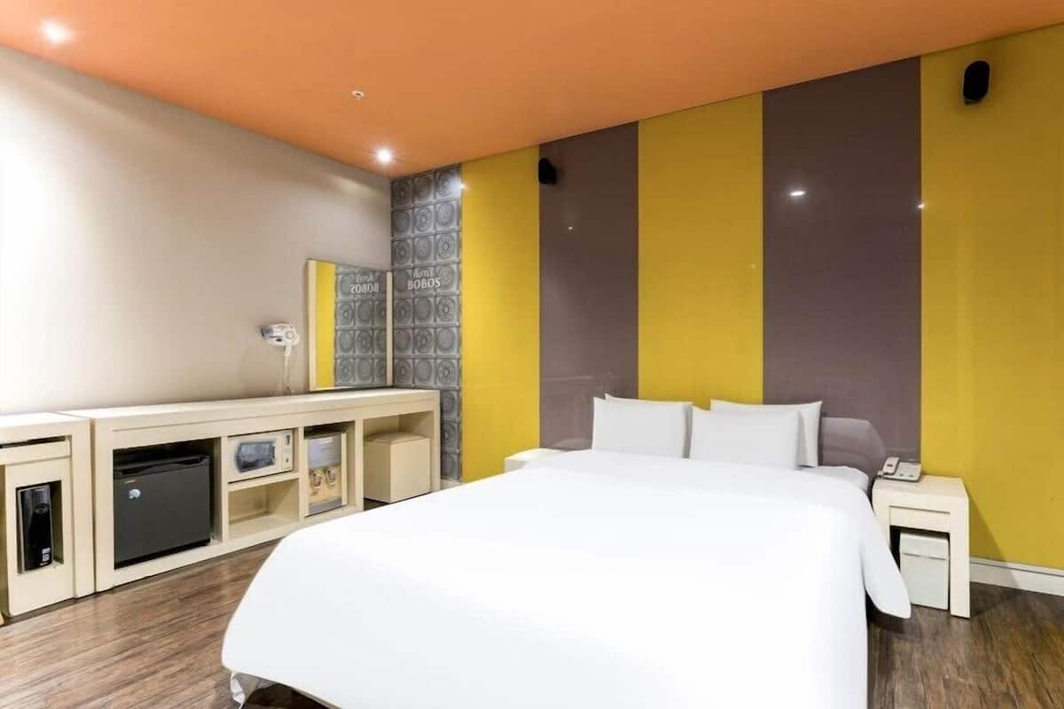 Une chambre d’hôtel comprenant un lit, des tables de chevet, un bureau avec un ordinateur et un petit réfrigérateur.