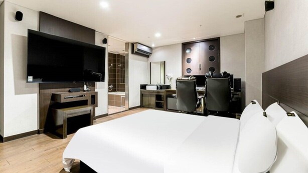 Ein modernes Hotelzimmer mit einem großen Bett, einem Flachbildfernseher, einem Schreibtisch mit zwei Stühlen und einer Duschkabine.