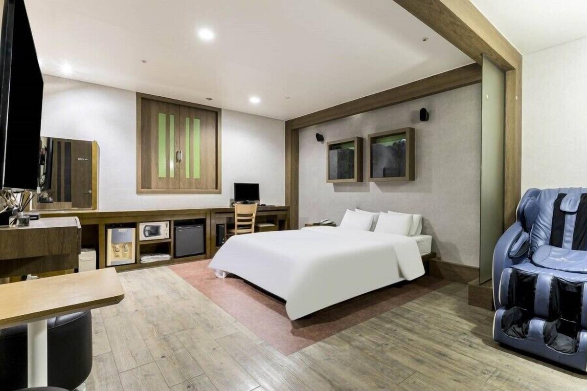Une chambre d’hôtel moderne dotée d’un grand lit, d’un fauteuil massant, d’un bureau avec un ordinateur et d’une petite kitchenette.