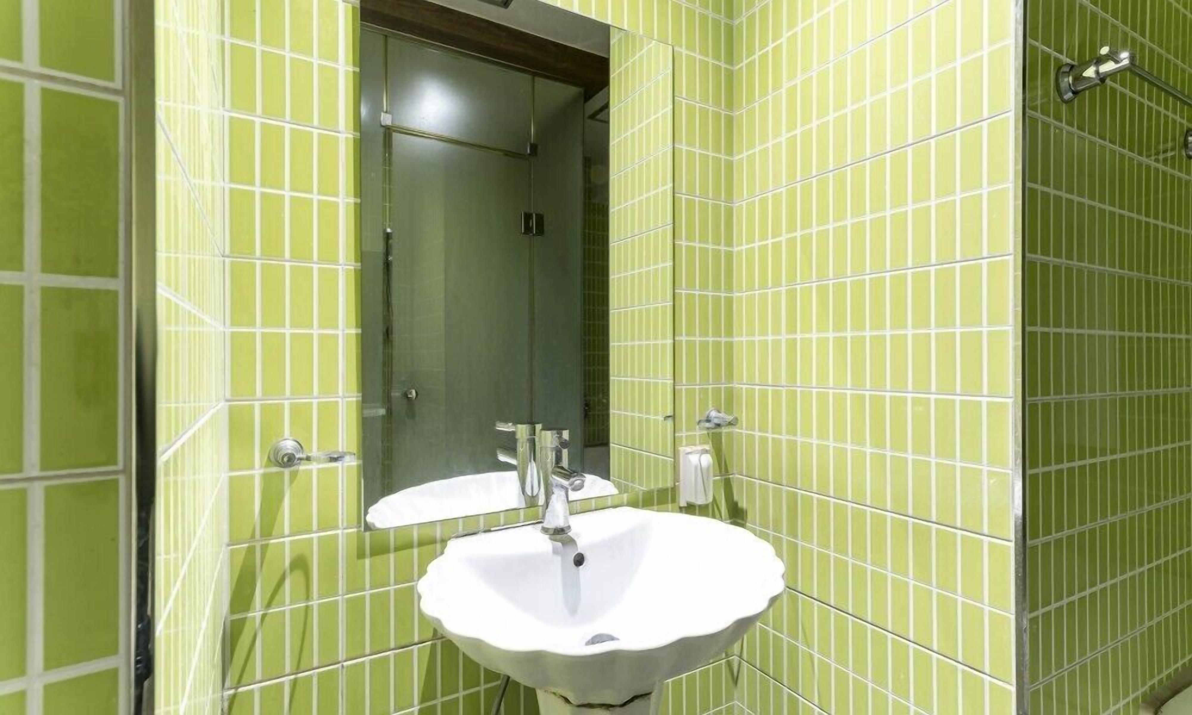 Un baño con paredes de azulejos verdes, un lavamanos blanco y un espejo.