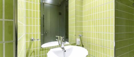 Un baño con paredes de azulejos verdes, un lavamanos blanco y un espejo.