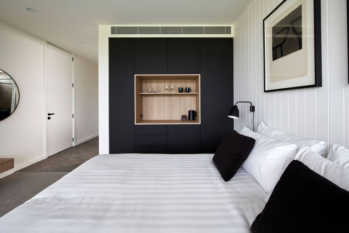 Un dormitorio moderno con una cama grande, una estantería empotrada con objetos y un cuadro enmarcado en la pared.