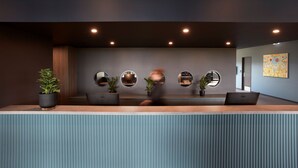 Un área de recepción moderna con mostrador de madera, plantas en macetas y espejos circulares en la pared.