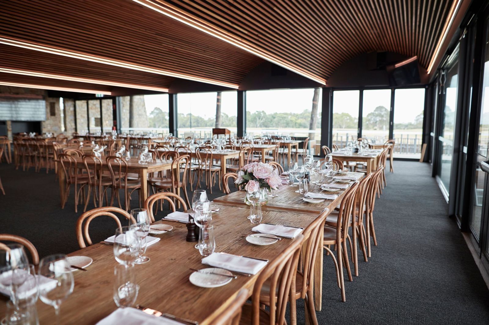 A large, open dining area with long wooden tables set for a formal event, featuring clear glassware and floral centerpieces.