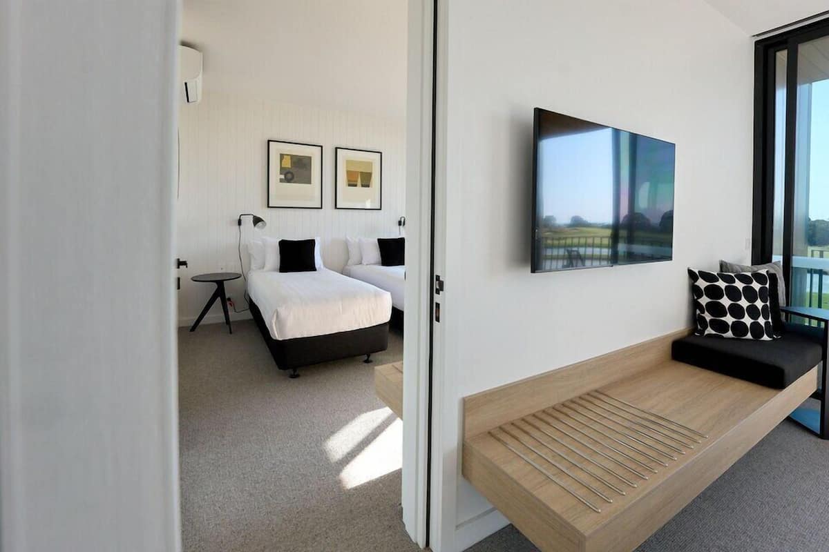 Una habitación de hotel moderna con una cama, una mesita pequeña, un banco y un ventanal grande.