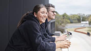 Two people in dark robes leaning on a balcony railing, holding a glass of wine.