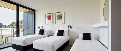 A modern hotel room with three single beds, a large window with a view of the outdoors, and a balcony.