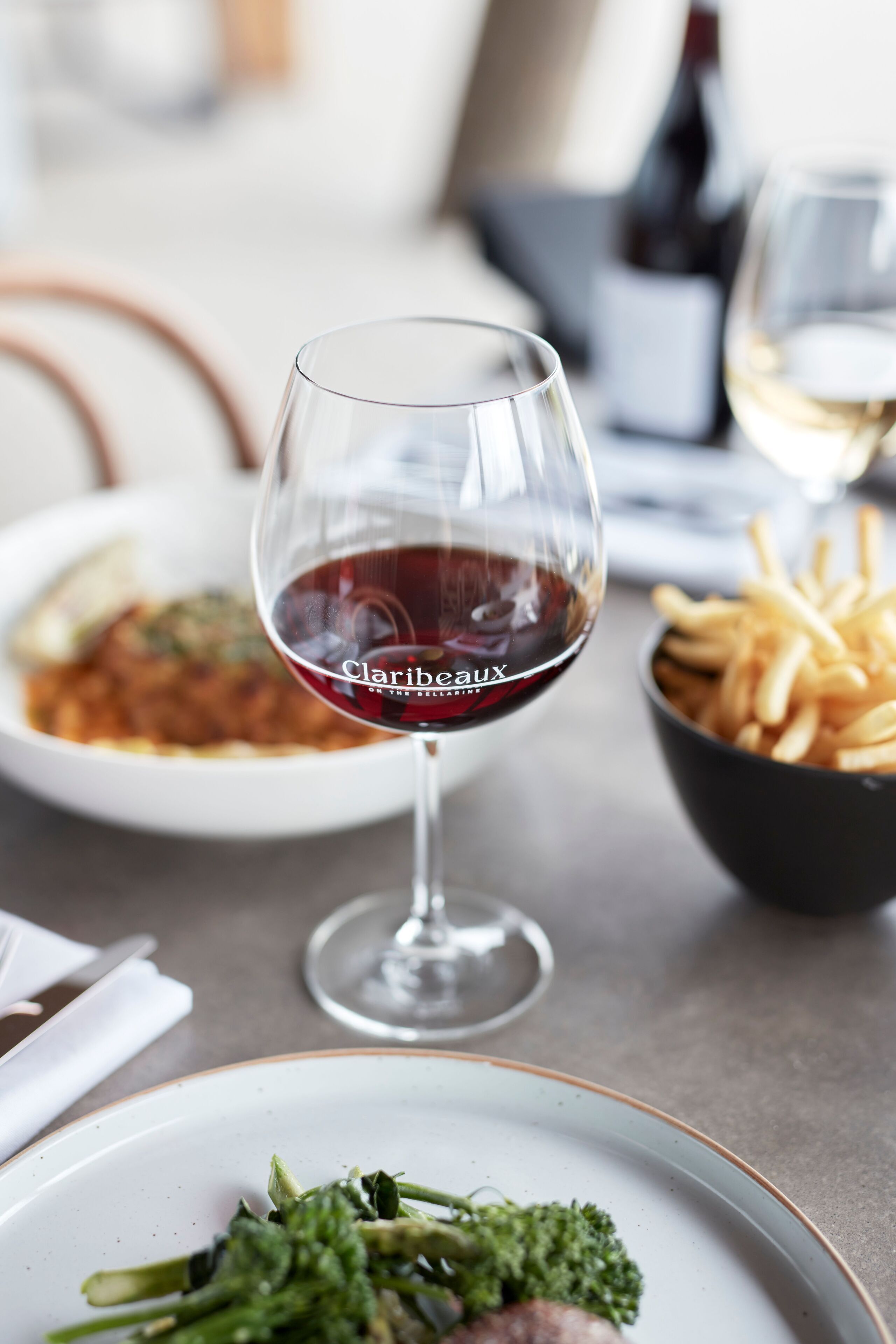 Una mesa de comedor con una copa de vino tinto, un bol de papas fritas y un plato de comida.